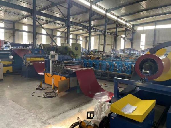 A wide shot of a factory floor showing a complete Hydraulic Coil Slitting Machine line, featuring a large red metal coil on a decoiler, feeding through rollers and slitting stations.