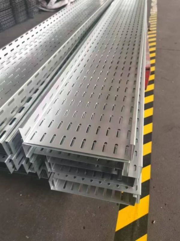Stacks of finished, perforated metal cable trays produced by the Fully Automatic Cable Tray Production Line, neatly arranged on a factory floor marked with yellow and black safety stripes.
