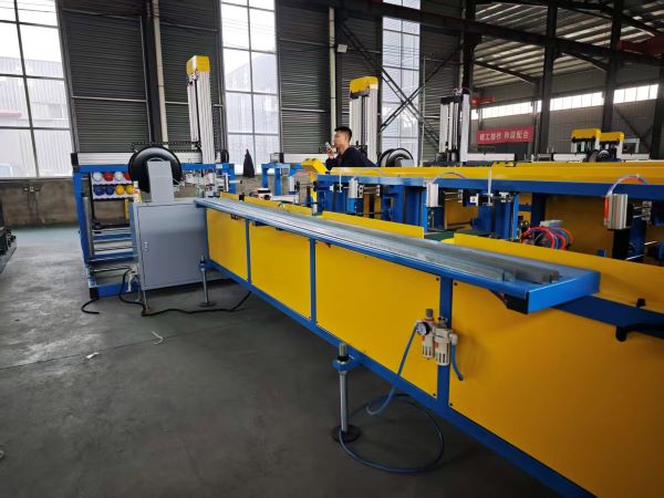 A long, yellow and blue industrial machine, identified as a Fully automatic light steel keel machine, is shown in a factory. A man is operating the controls in the background, and a formed metal keel rests on the machine's output table.