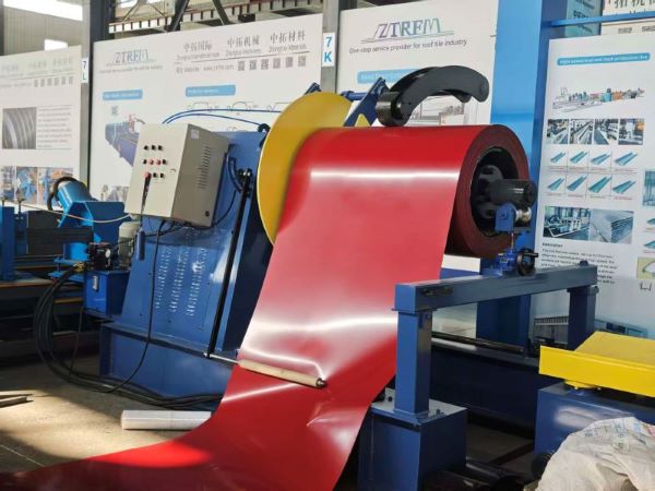 A red pre-painted steel coil being unwound on the decoiler of a hydraulic slitting line, with the sheet metal feeding into the processing machinery.