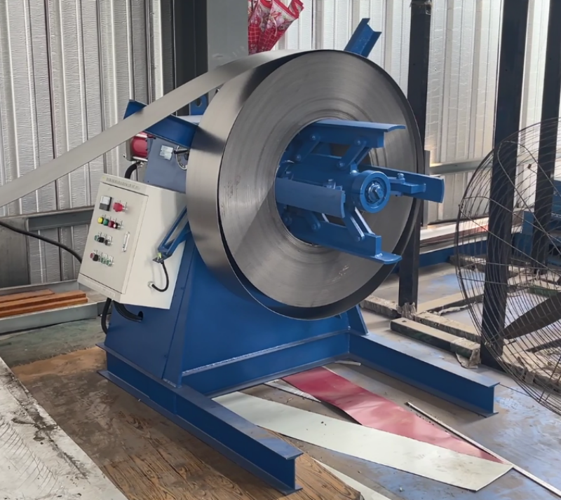 A blue decoiler machine holding a large steel coil, feeding a metal strip into a production line, with a control box mounted on the side.
