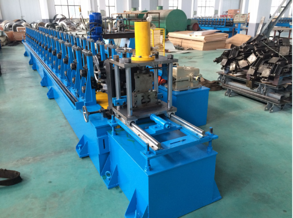 A long, blue industrial machine, identified as an upright pillar production line, situated in a factory workshop with various metal components and machinery in the background.