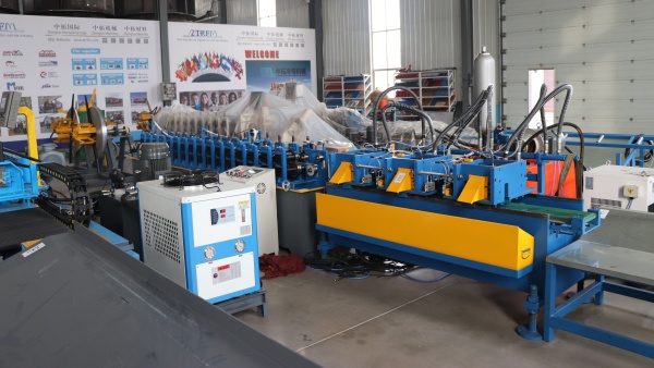 Wall Angle Roll Forming Machine in a factory, showing the blue and yellow main unit with a white cooling unit and control panel.