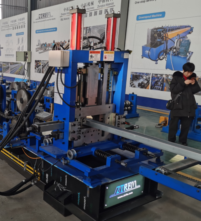 Cutting system of a CZ purlin making machine, showing hydraulic press and blade assembly mounted on blue frame with formed profile exiting below.
