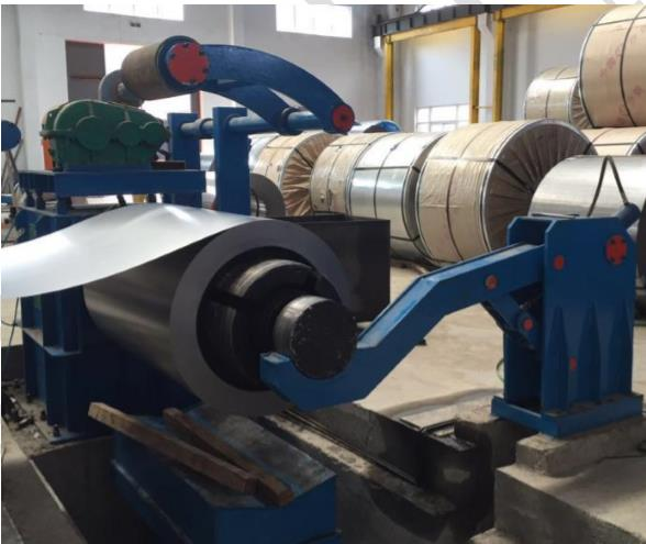 Blue hydraulic decoiler in operation, feeding metal strip into a hydraulic slitting line within an industrial workshop.