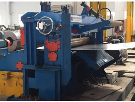 Blue hydraulic press and pinch device in operation, guiding metal strip through a hydraulic slitting line within an industrial workshop.