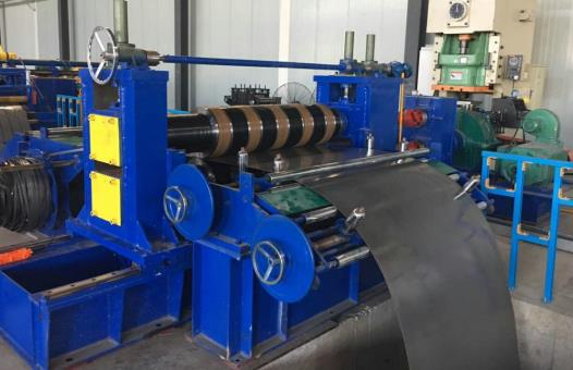 Blue slitter unit in operation, processing metal strip as part of a hydraulic slitting line within an industrial workshop.